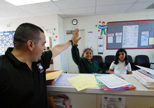 Virginia Rocca Barton Elementary School Principal Jose Juan Urquizo high-fives student Michelle Becerra, who is turning in good behavior points at the front desk.